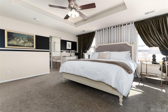 carpeted bedroom featuring visible vents, baseboards, a ceiling fan, ensuite bathroom, and a tray ceiling