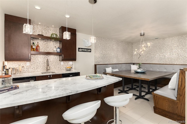 kitchen with light stone countertops, dark brown cabinetry, a kitchen breakfast bar, and a sink