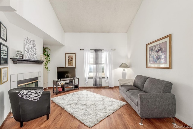 living room with baseboards, high vaulted ceiling, wood finished floors, and a tiled fireplace