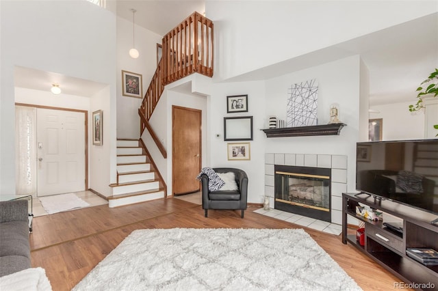 living area featuring a tile fireplace, stairs, a high ceiling, and wood finished floors