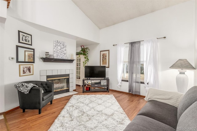 living area with baseboards, high vaulted ceiling, wood finished floors, and a tiled fireplace