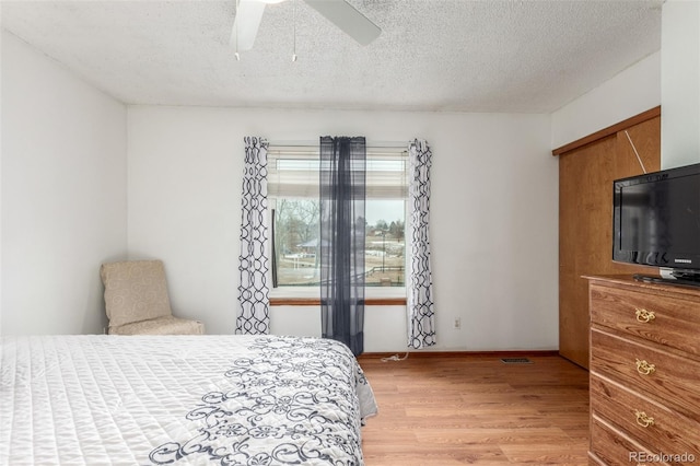 bedroom with light wood-type flooring, visible vents, a textured ceiling, baseboards, and ceiling fan