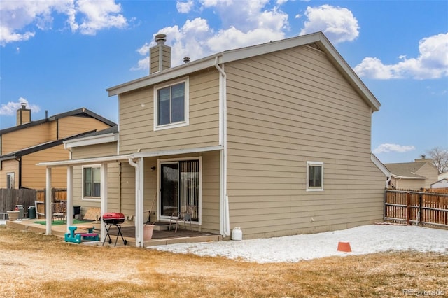 rear view of house featuring a patio, fence, and a chimney