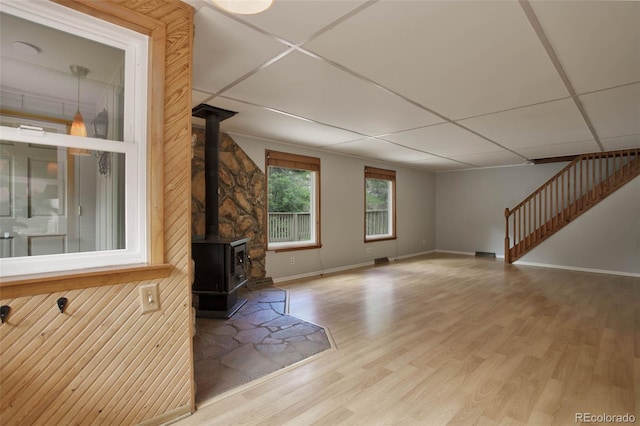 unfurnished living room with a paneled ceiling, light hardwood / wood-style floors, and a wood stove