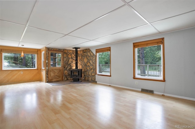 unfurnished living room with light hardwood / wood-style flooring, a wood stove, and a drop ceiling