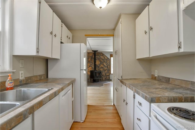 kitchen with white dishwasher, sink, white cabinets, light hardwood / wood-style floors, and a wood stove