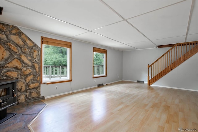 unfurnished living room with a paneled ceiling, light hardwood / wood-style floors, and a wood stove