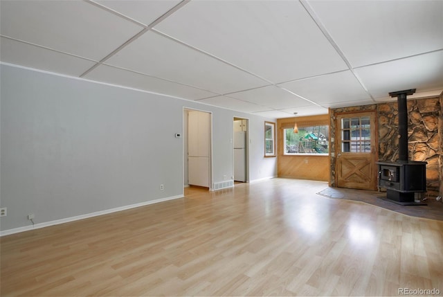 unfurnished living room with light wood-type flooring, a wood stove, and a paneled ceiling