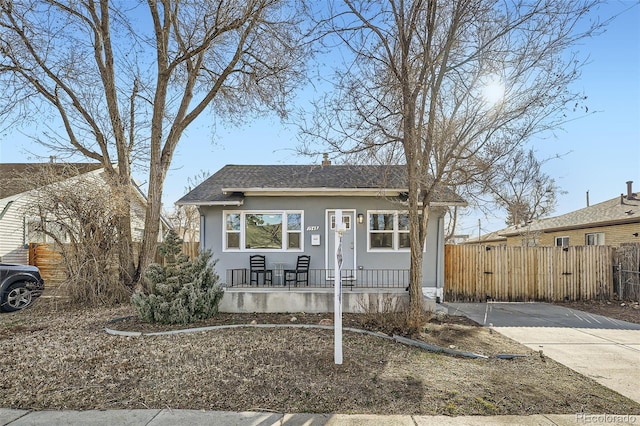 bungalow-style home with a shingled roof, a porch, fence, and stucco siding