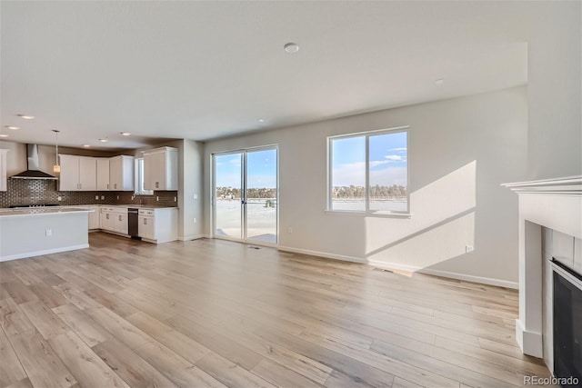 unfurnished living room with recessed lighting, light wood finished floors, baseboards, and a glass covered fireplace
