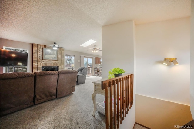 carpeted living area featuring ceiling fan, a brick fireplace, a skylight, and a textured ceiling