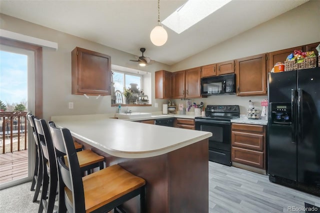 kitchen featuring a kitchen bar, light countertops, vaulted ceiling with skylight, a peninsula, and black appliances