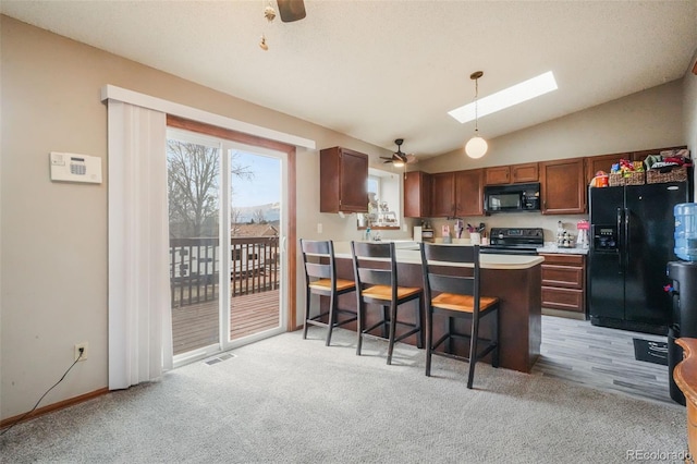 kitchen with vaulted ceiling with skylight, a peninsula, black appliances, and ceiling fan