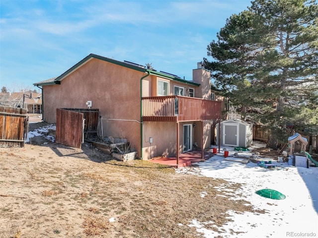 back of property with a storage unit, stucco siding, a deck, an outdoor structure, and a chimney