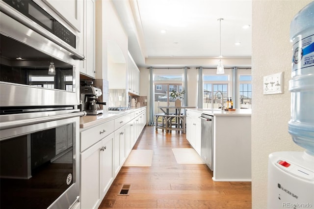 kitchen with hanging light fixtures, stainless steel appliances, light hardwood / wood-style floors, decorative backsplash, and white cabinets