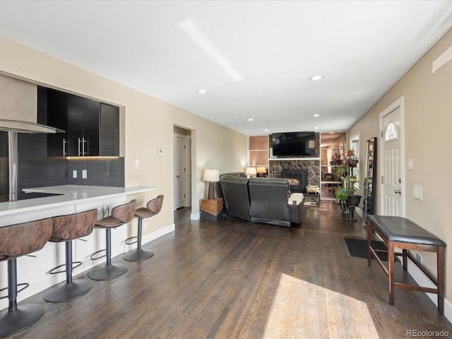 living room featuring a stone fireplace, dark wood finished floors, recessed lighting, and baseboards