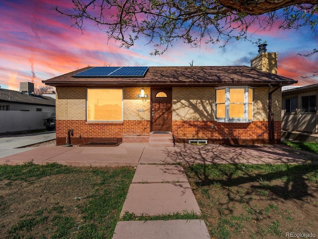 ranch-style house with brick siding, entry steps, roof mounted solar panels, a chimney, and cooling unit