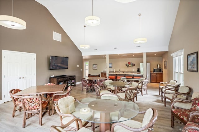 dining area with visible vents, light wood-style flooring, high vaulted ceiling, and baseboards