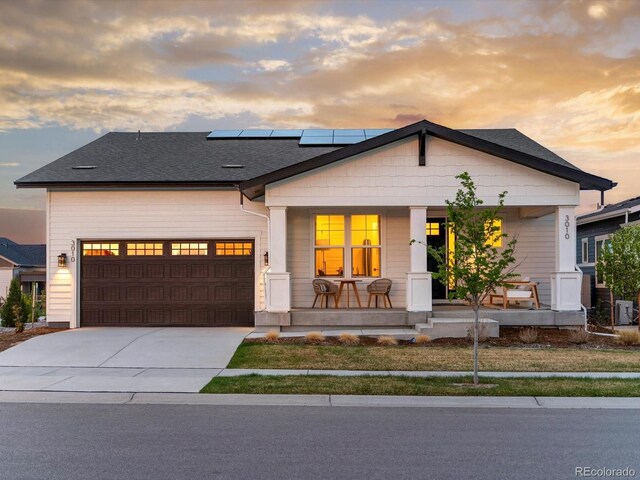 view of front facade with a porch, concrete driveway, an attached garage, and solar panels