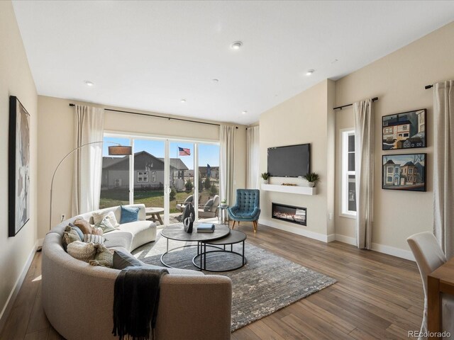 living room featuring baseboards, a glass covered fireplace, and wood finished floors