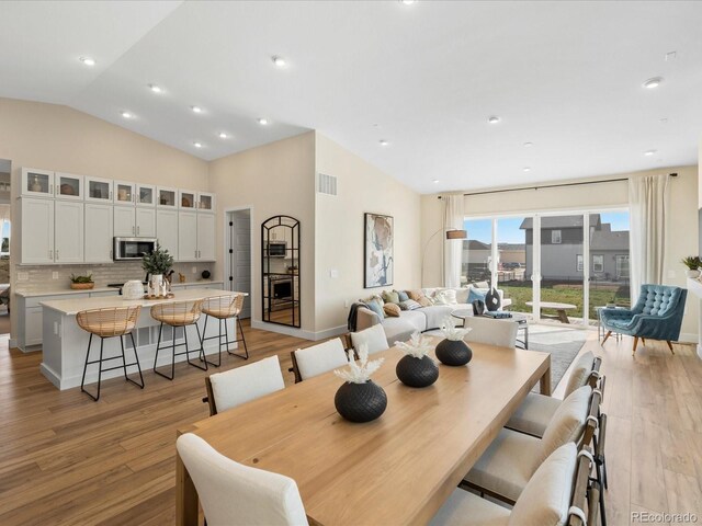 dining space with baseboards, lofted ceiling, light wood-type flooring, and visible vents