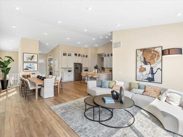 living room with recessed lighting, visible vents, vaulted ceiling, and light wood-type flooring