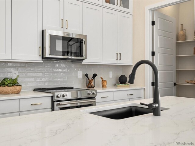 kitchen featuring light stone countertops, a sink, stainless steel appliances, white cabinetry, and decorative backsplash
