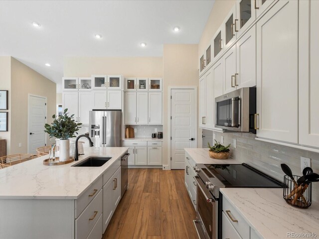 kitchen with wood-type flooring, an island with sink, a sink, backsplash, and stainless steel appliances