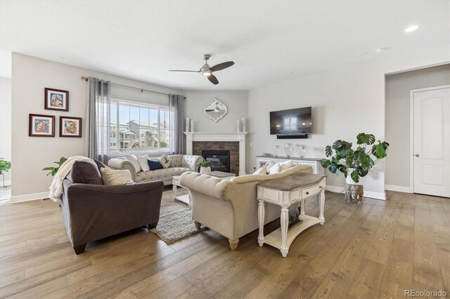 living room featuring a ceiling fan, hardwood / wood-style floors, a stone fireplace, baseboards, and recessed lighting
