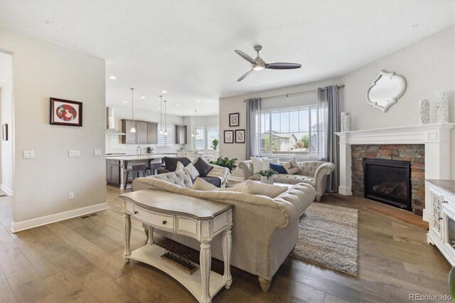 living room with hardwood / wood-style flooring, ceiling fan, a stone fireplace, recessed lighting, and baseboards