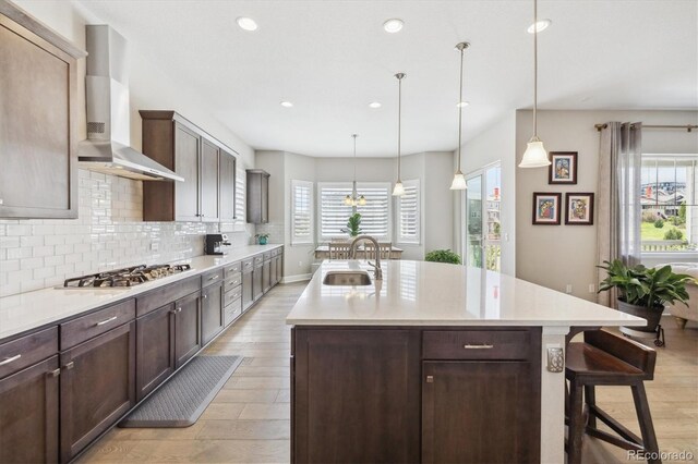 kitchen with a sink, stainless steel gas cooktop, wall chimney range hood, light wood-type flooring, and backsplash