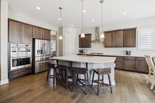 kitchen featuring appliances with stainless steel finishes, wall chimney range hood, dark wood finished floors, backsplash, and recessed lighting