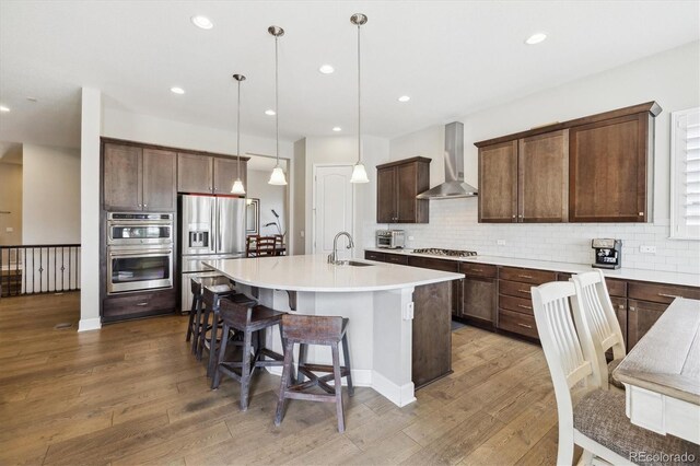 kitchen with wall chimney range hood, stainless steel appliances, wood finished floors, tasteful backsplash, and recessed lighting