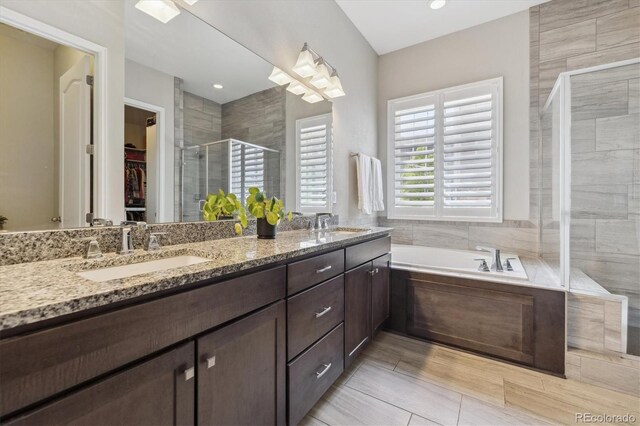 bathroom with a shower stall, a walk in closet, double vanity, and a garden tub