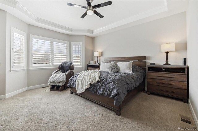 carpeted bedroom featuring a tray ceiling, crown molding, baseboards, and a ceiling fan