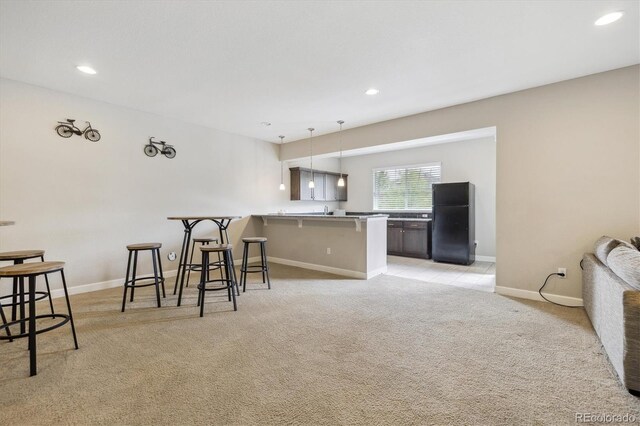 kitchen featuring freestanding refrigerator, a kitchen breakfast bar, light carpet, a peninsula, and hanging light fixtures