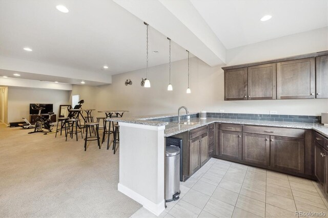 kitchen featuring a peninsula, dark brown cabinets, light stone counters, and recessed lighting