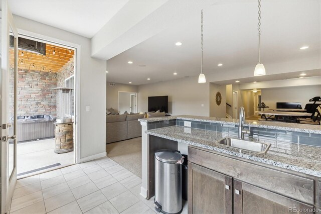 kitchen with a sink, open floor plan, light tile patterned floors, pendant lighting, and light stone countertops