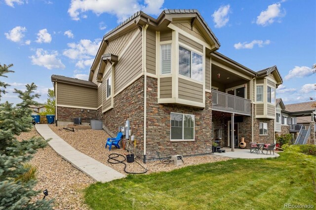 rear view of property featuring a balcony, stone siding, a lawn, and a patio area