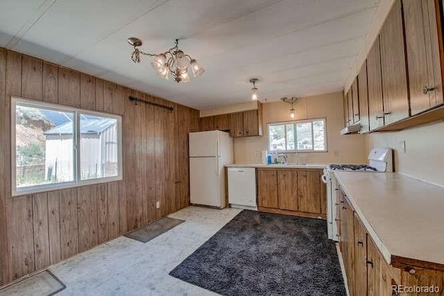 kitchen with wood walls, sink, a chandelier, and white appliances