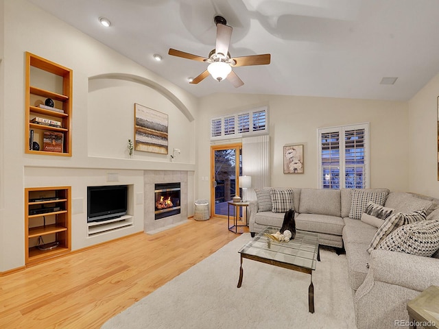 living room featuring built in shelves, vaulted ceiling, ceiling fan, hardwood / wood-style flooring, and a fireplace