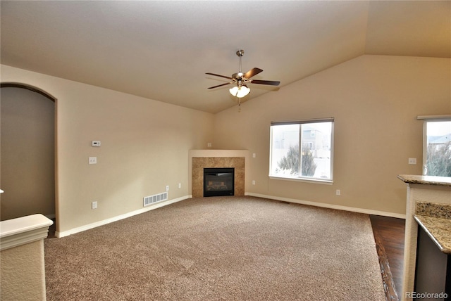 unfurnished living room with lofted ceiling, ceiling fan, dark colored carpet, and a fireplace