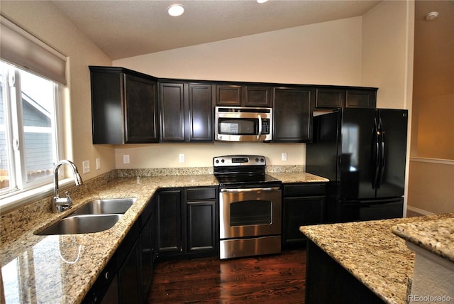 kitchen featuring sink, stainless steel appliances, vaulted ceiling, and light stone counters