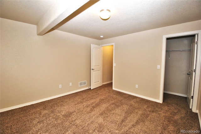 unfurnished bedroom with a closet, dark colored carpet, a spacious closet, and a textured ceiling