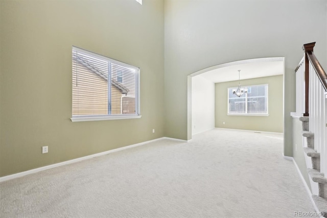 spare room featuring a towering ceiling, light colored carpet, and an inviting chandelier