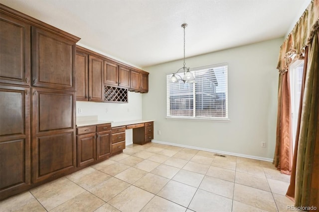 kitchen featuring light tile patterned flooring, pendant lighting, dark brown cabinets, and built in desk