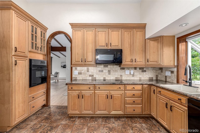 kitchen featuring tasteful backsplash, a sink, black appliances, dark stone countertops, and glass insert cabinets