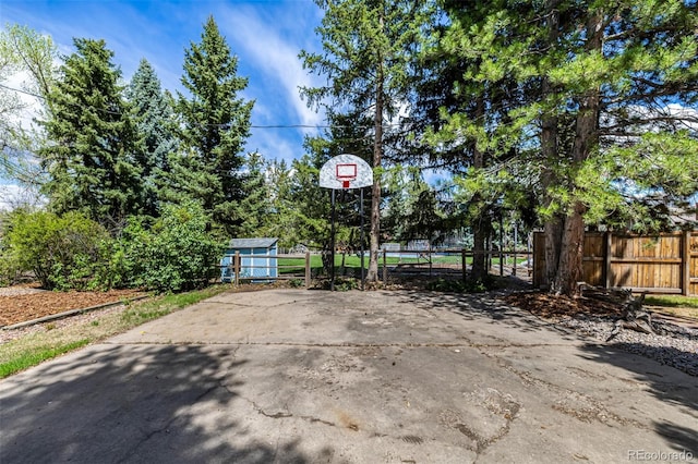 view of patio featuring fence, basketball court, an outbuilding, and a storage unit
