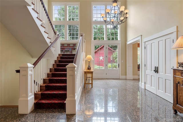 entryway with granite finish floor, baseboards, a notable chandelier, a high ceiling, and stairs