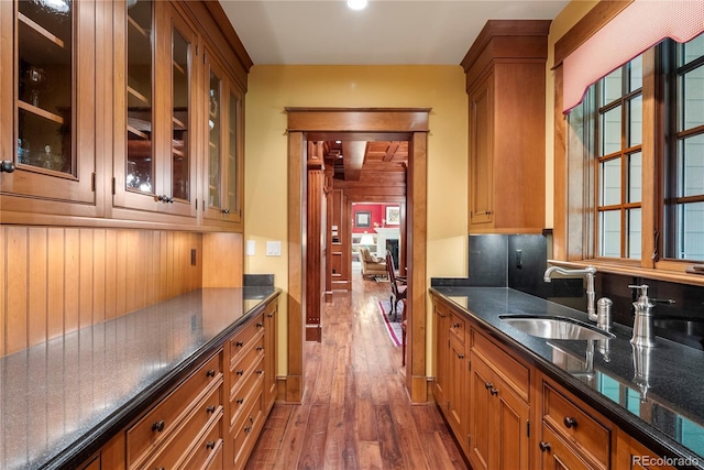 kitchen featuring glass insert cabinets, a sink, brown cabinets, and dark wood-style flooring